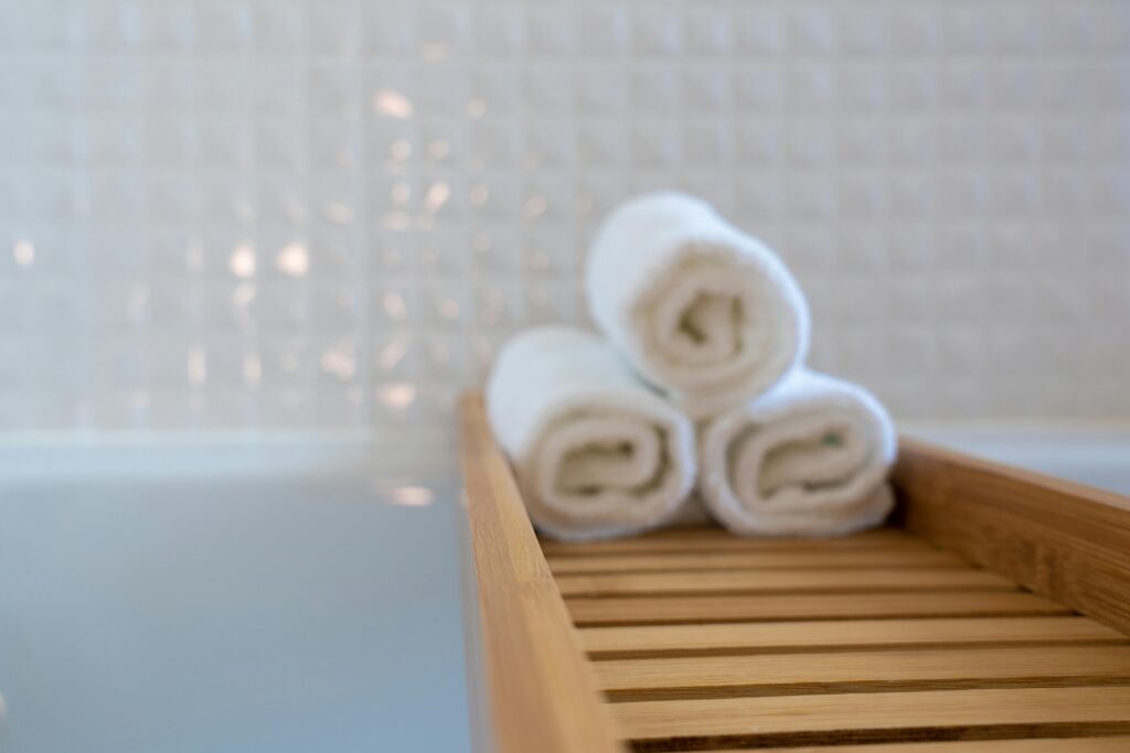 A close-up of rolled white towels on a wooden bath tray in a modern bathroom.