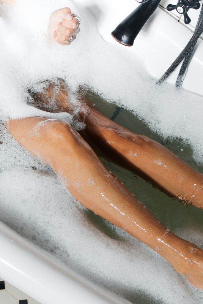 A woman enjoying a calming bubble bath with visible legs, promoting relaxation and self-care.