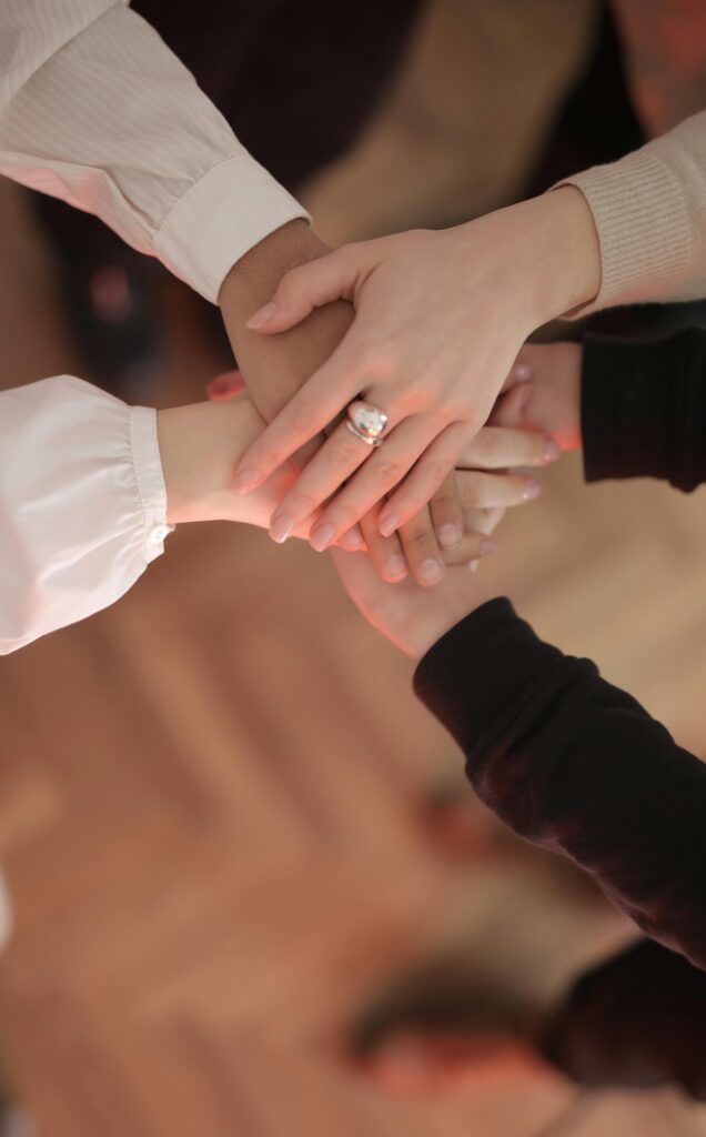 pexels-photo-3830752-3830752 Top view of faceless friends in different clothes stacking hands together while standing on wooden floor indoor on sunny day